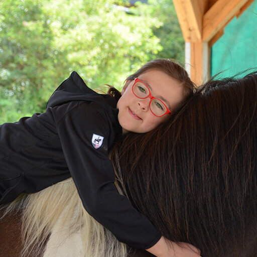 Ein Kind liegt auf dem Rücken des Pferds um die Körperwahrnehmung weiterzuentwickeln